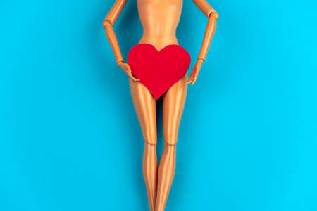 legs of a plastic doll with a red heart covering the crotch on a vibrant blue background