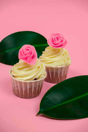 sweet cupcakes decorated with roses and tropical leaves on a pastel pink background selective focus