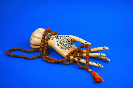 wooden hand holds a rosary on a bright blue background
