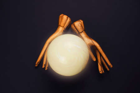 creative esoteric still life with a ball of predictions and two wooden female hands on  black...