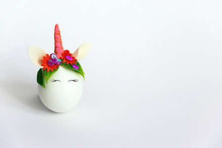 cute spring Easter card with an unicorn egg with a rim of spring flowers and horn  with copy space on a white backgroundの写真素材