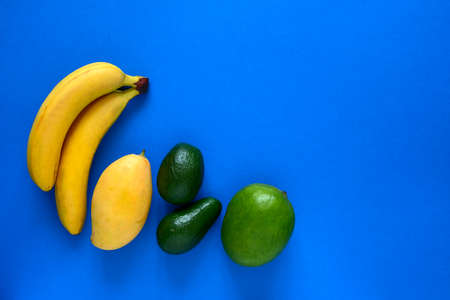 top view layout of  fresh bananas,mangoes and avocado on a blue background with place for textの写真素材