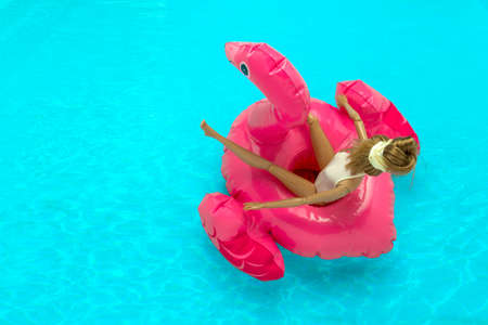 summer vacation concept plastic doll floating on inflatable pink flamingo on a background of blue waterの写真素材