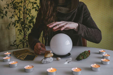 young mysterious woman holds her hands over a crystal ball of predictions