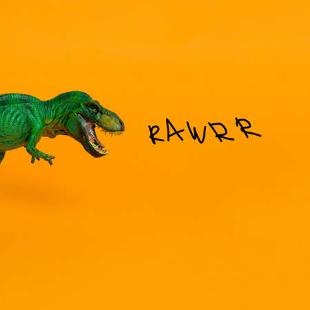 green dinosaur with open mouth and inscription rawrr on bright orange backgroundの写真素材