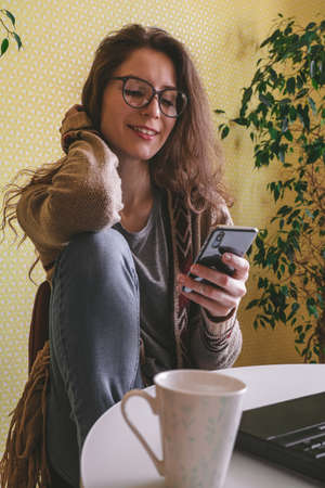 beautiful caucasian woman using mobile phone and sitting at the table with laptop and coffee cupの写真素材