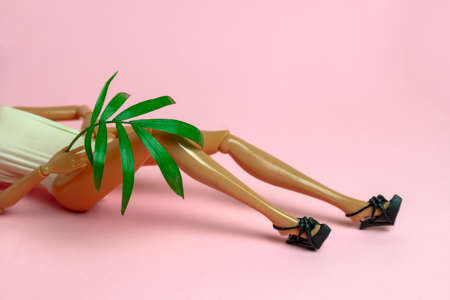 close up   plastic doll lying on a pink background holding a palm leaf, copy spaceの写真素材