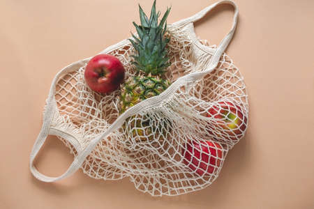 top view flat lay string bag with pineapple and red apples on a beige background