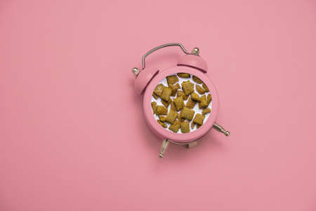 top view flat lay pink alarm clock with a breakfast of crunchy pillows and milk inside on a pink...