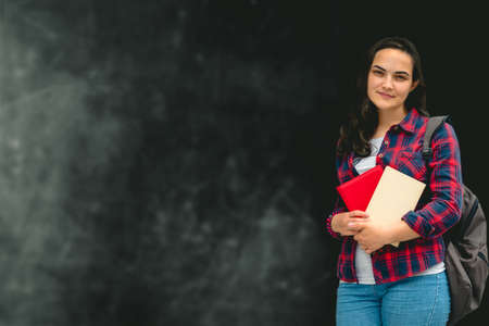 curly woman wearing casual shirt and jeans and backpack  holding books on a background of chalkboard...