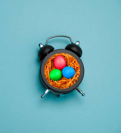 black alarm clock with spring colorful easter eggs inside on a blue background, happy easter card...