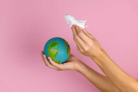 female hands holding white plane and little earth on a pink background,travel conceptの写真素材
