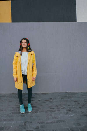 beautiful young sad lady using headphones and listening music against gray wall outdoor copy spaceの写真素材