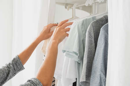 close up female hands and basic women's clothes on a hanger, open wardrobe with textile curtains...