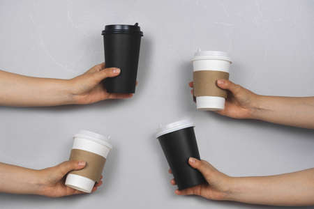 hands with takeaway drink cups on a gray concrete wall background