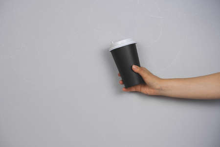 female hand holding coffee to go blank cup against concrete gray wall copy spaceの写真素材
