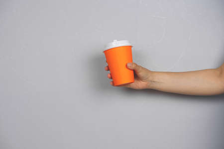 female hand holding coffee to go blank cup against concrete gray wall copy space