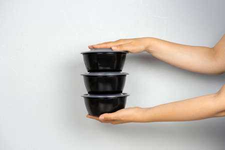 female hands holding ready meal in black containers against gray wall, delivery concept