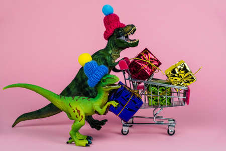 two cute dinosaurs in knitted hats with shopping trolley full of present boxes, sale conceptの写真素材