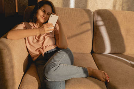 healthy young beautiful woman in casual clothes using smartphone and sitting on a sofaの写真素材