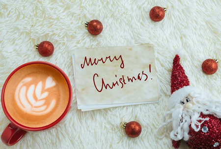 top view red cup of cappuccino and Santa Claus toy on a background of fluffy white blanket with...
