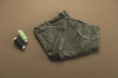 top view of a piece of fabric and a spool of thread on a brown background