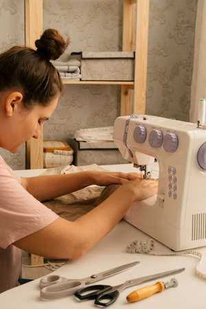 young beautiful caucasian woman sews on a sewing machine, hobby and sewing production conceptの写真素材