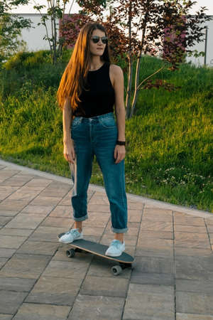 young brunette woman riding skateboard at the park in the summer