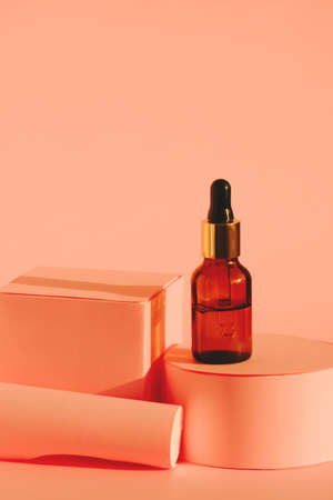 glass bottle with cosmetic product with pipette on a pink pedestal on a pink backgroundの写真素材