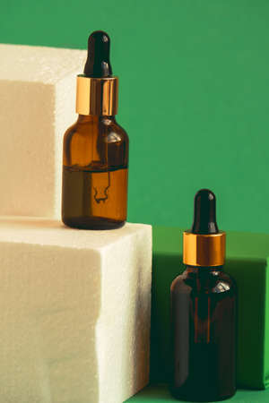 glass bottle with cosmetic product with pipette on a green pedestal on a green backgroundの写真素材