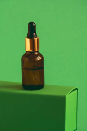 glass bottle with cosmetic product with pipette on a green pedestal on a green backgroundの写真素材
