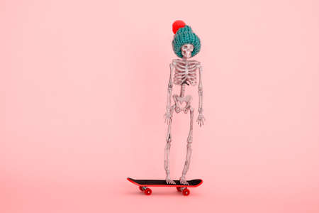skeleton wearing knitted hat riding on skateboard against pastel pink backgroundの写真素材