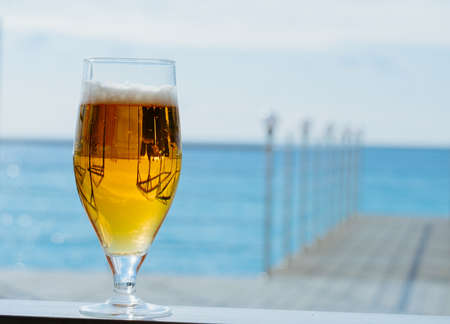 fresh cold glass of beer on a sea restaurant terrace in a sunny day, copy space blurred backgroundの写真素材