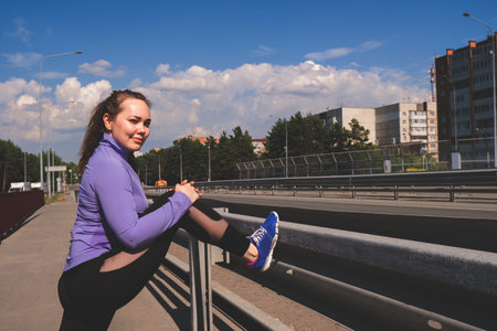 young athletic girl stands with her foot on the railing of the bridge, workout urban sport concept