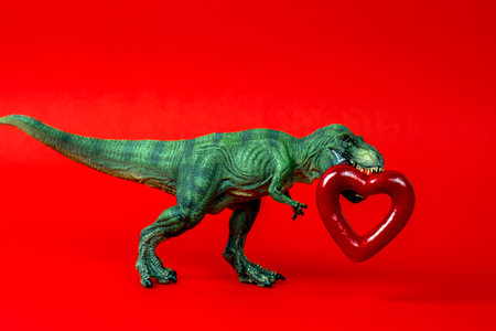 Green cute dinosaur with red heart on a red background. Creative minimal greeting card on Valentines day. Love concept.の写真素材