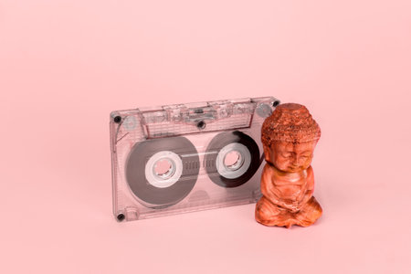 Audio tape and Buddha figurine on a pink background. Music playlist for yoga and meditation concept. Selective focus.の写真素材