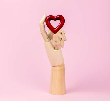 Human wooden hand model with red heart on pastel pink. Heart health concept.の写真素材