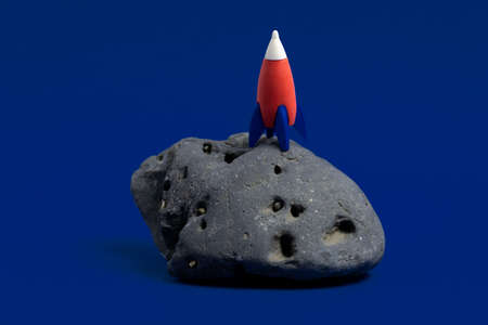 Cute miniature rocket on a moon stone on a dark blue background. Minimal space day card.の写真素材