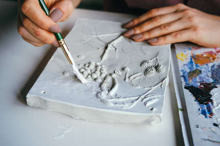 Female hands close-up works with plaster relief and white paint. DIY and hobby concept.の写真素材