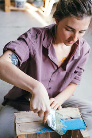 Beautiful young woman painting wooden box. DIY and hobby concept.の写真素材