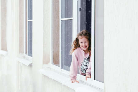 Happy young girl positive portrait. Happy kid sitting on the windowsill and enjoying good winter...
