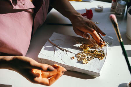 Close-up female hands working with plaster relief and golden foil. DIY and art hobby concept.
