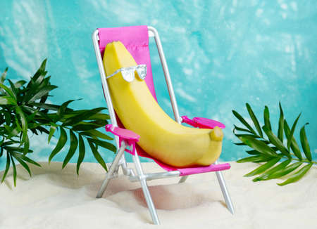 Banana in sunglasses relaxes on a beach chair. Summer tropical minimal humor poster.