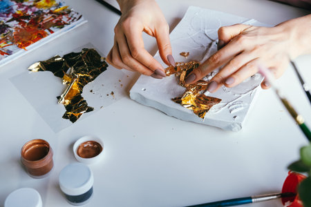 Close-up female hands working with plaster relief and golden foil. DIY and art hobby concept.の写真素材