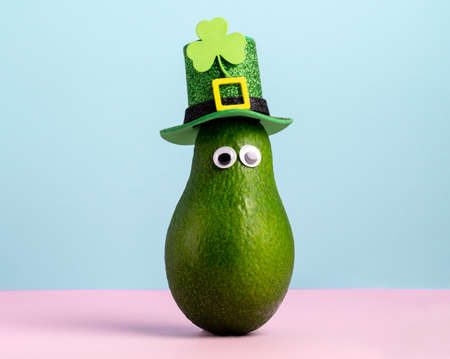 Cute st. Patrick card with avocado in hat pastel pink and blue backgroundの写真素材