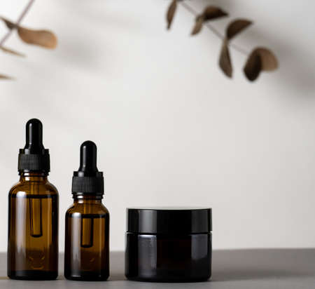 Cosmetic product brown glass jar with eucalyptus dry leaves on a gray background, copy space.の写真素材