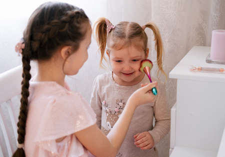 The older sister does makeup for the younger sister. Cute family children's lifestyle.の写真素材