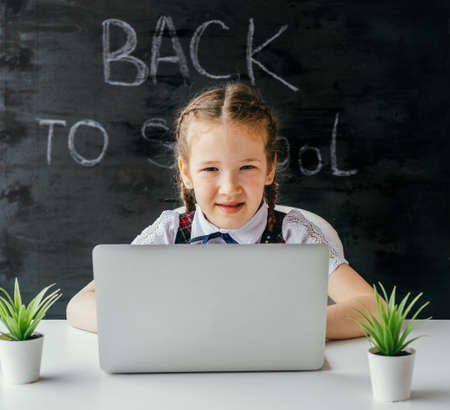 Cute little school girl sitting at the desk and using computer. Back to school and online lessons concept.の写真素材