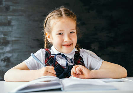 Portrait beautiful positive little schoolgirl sitting at her desk and doing her homework. Back to...