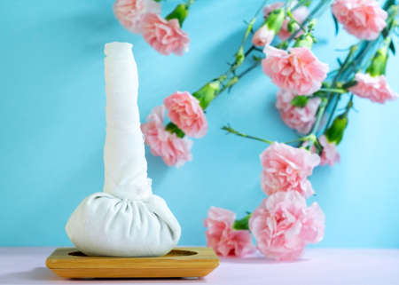 Herbal spa bag on blue background with pink carnations. Ayurvedic spa treatments advertising poster conceptの写真素材